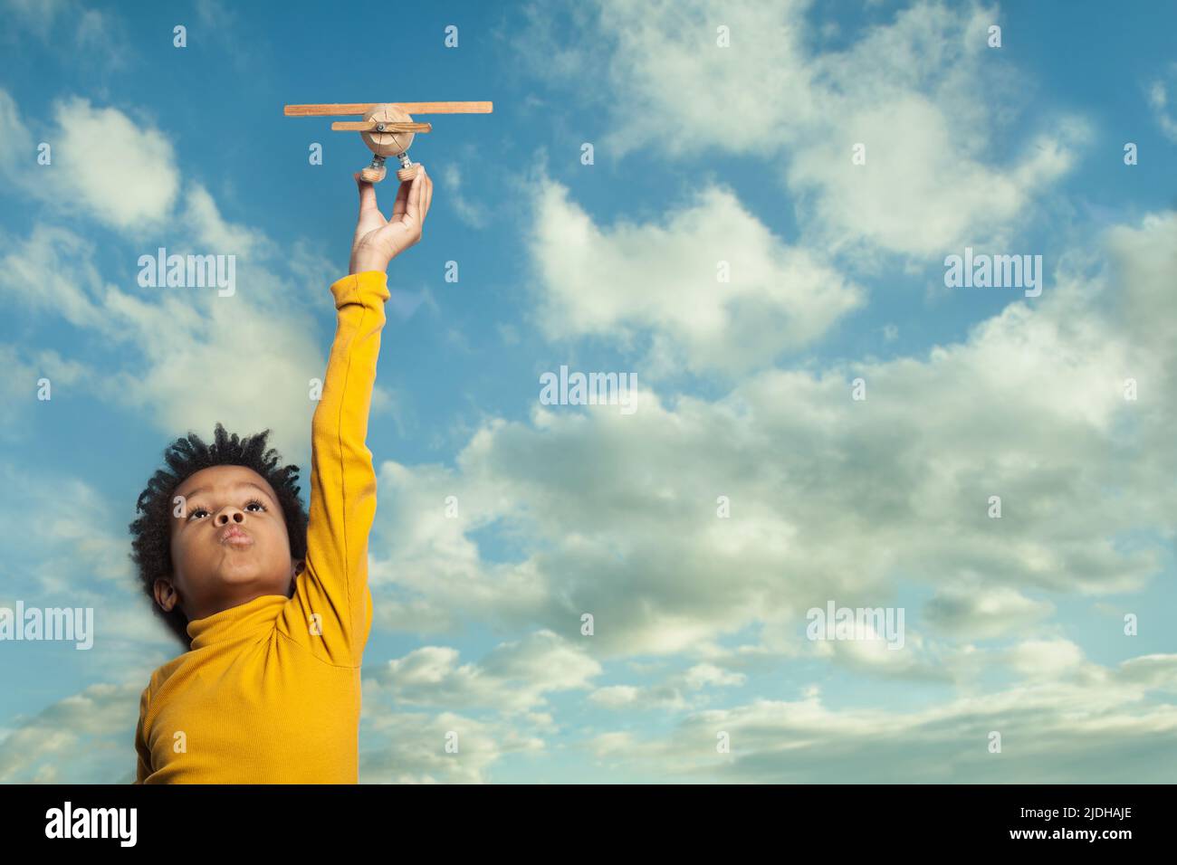Curious small black child boy with airplane against blue sky clouds background Stock Photo