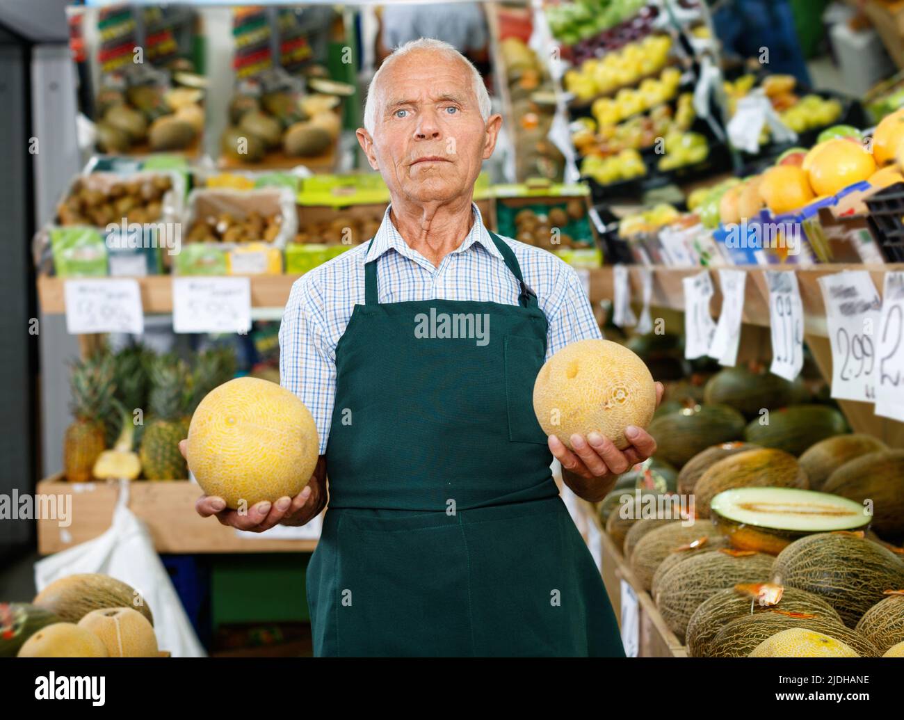 Positive senior male owner of greengrocery shop in apron offering fresh