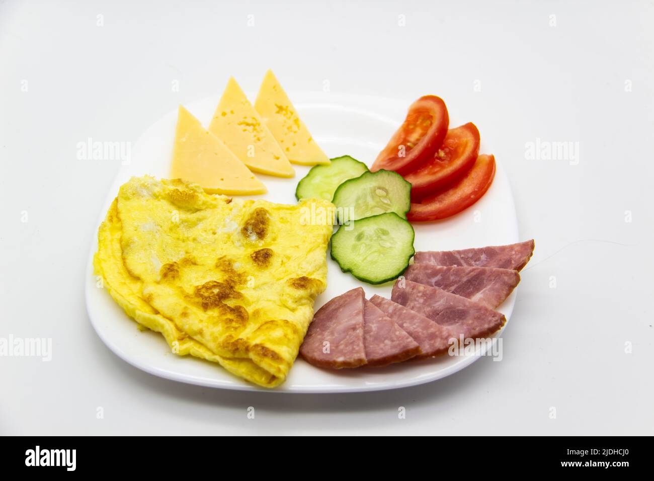 Tasty breakfast or lunch with omelet with sausage, tomato, cucumber, and pieces of cheese on the white plate. Stock Photo