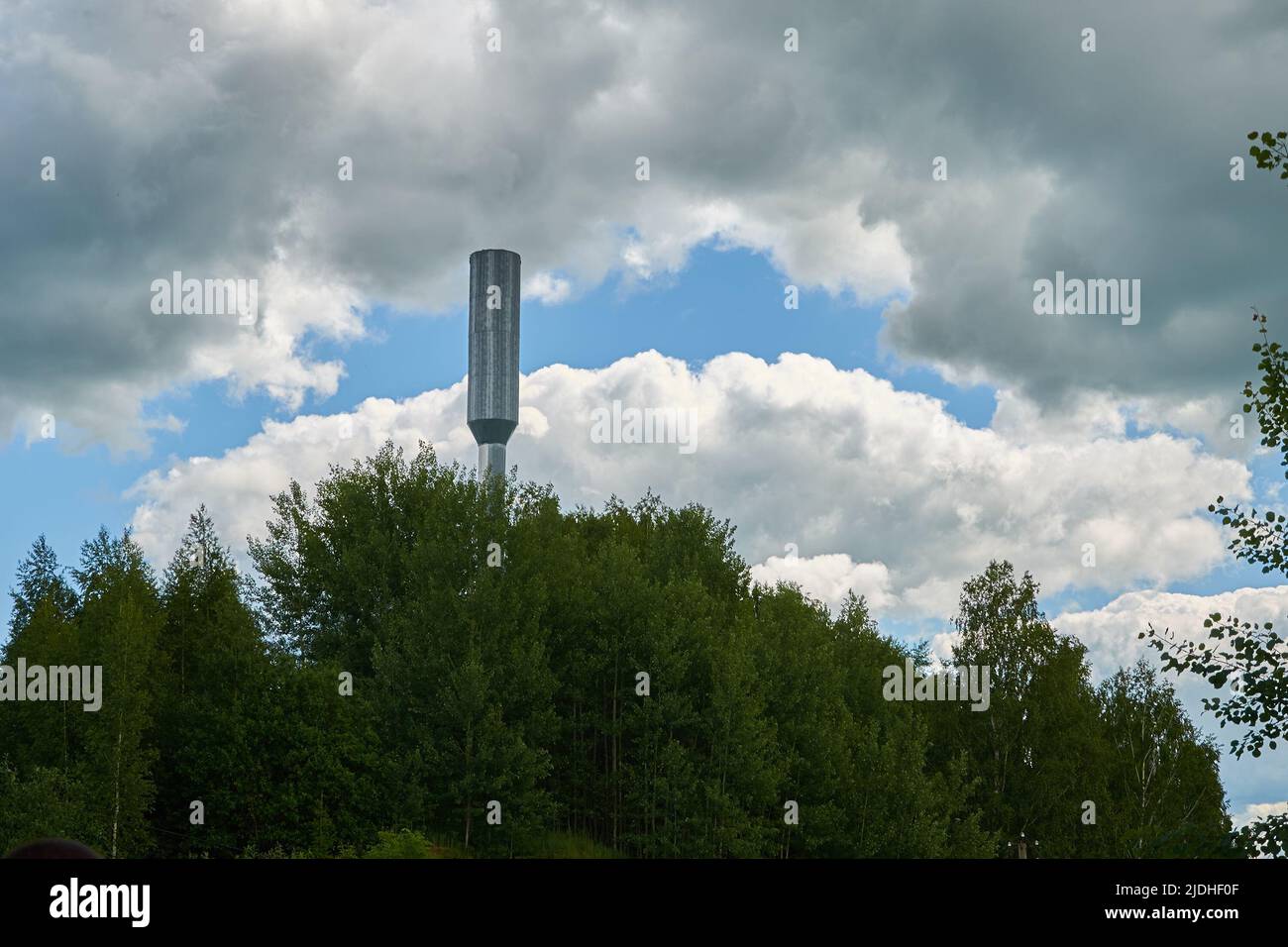 Metal water tower on a background of cloudy sky and trees Stock Photo