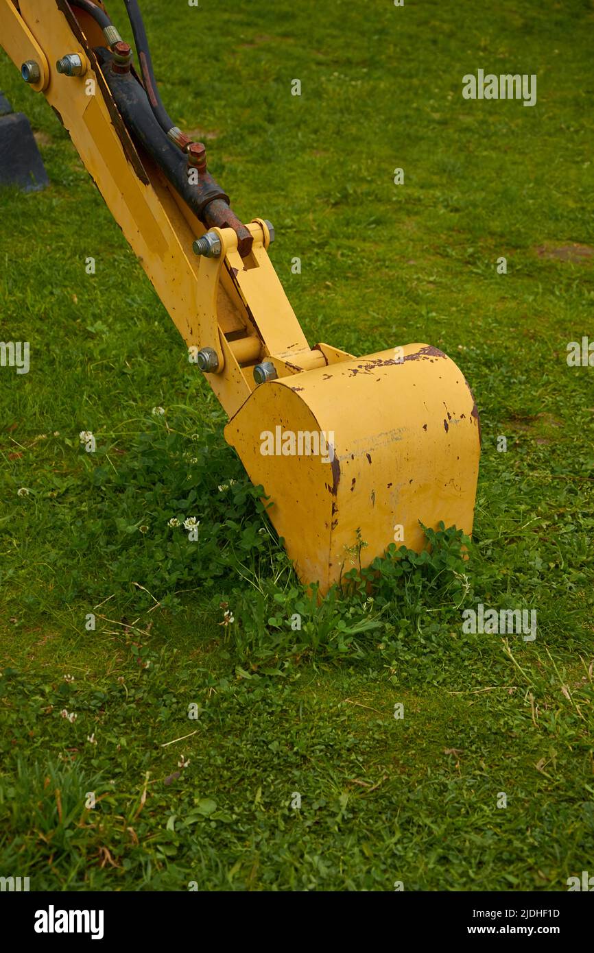 The bucket of the yellow excavator is lying on the lawn. Vertical format Stock Photo