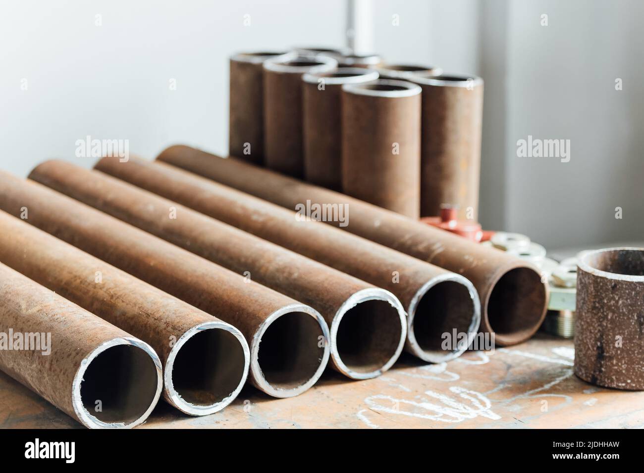 Round metal pipes of same diameter lie in row on workbench in industrial workshop. Manufacture and production of metal products. Industrial background. Stock Photo