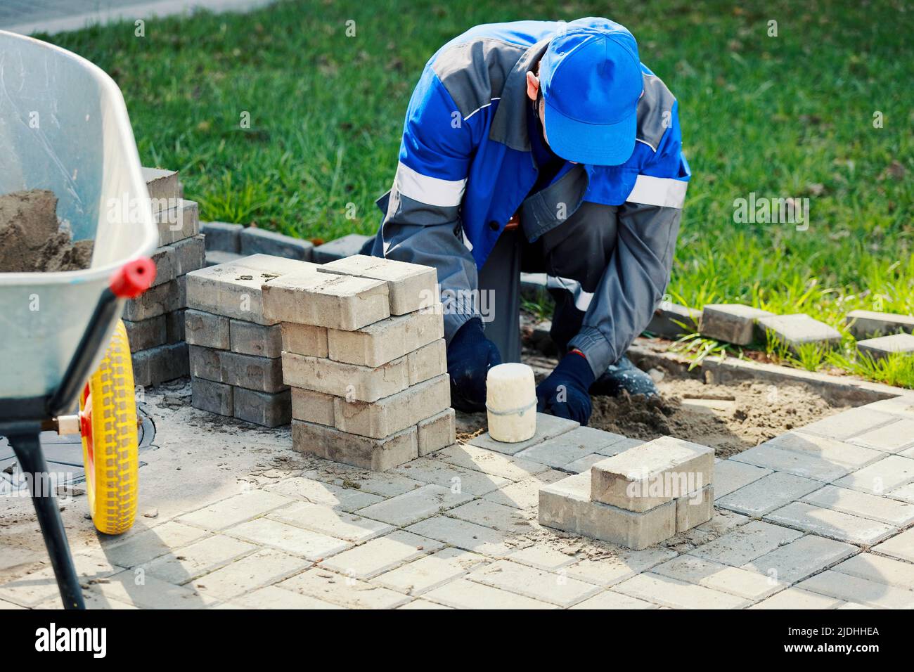 Bricklayer lays paving slabs outside. Working man performs landscaping. Builder lays out sidewalk with stone blocks. Authentic workflow. Hard work in old age. Stock Photo