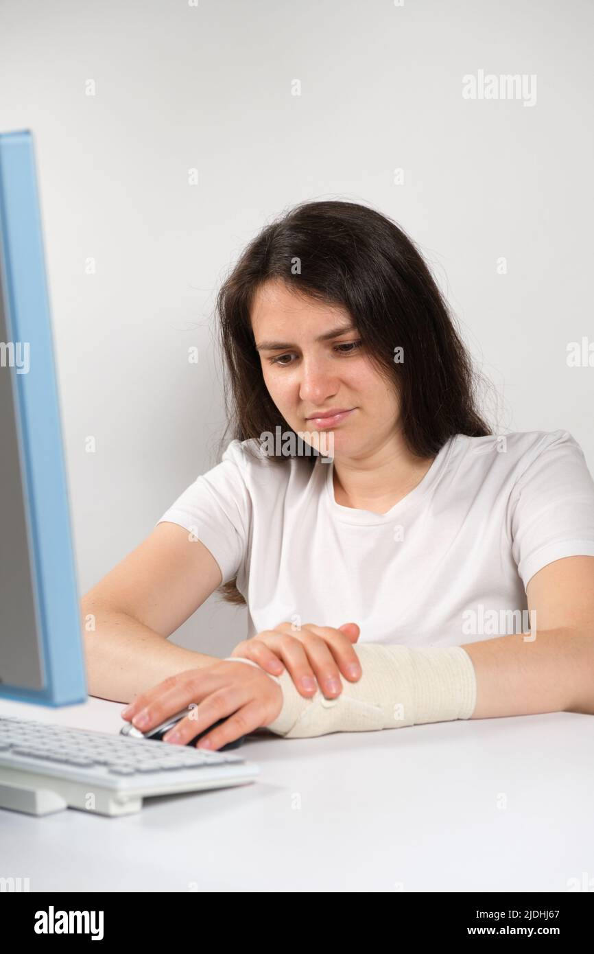 A woman with an elastic bandage on her wrist sits in front of a computer, carpal tunnel syndrome