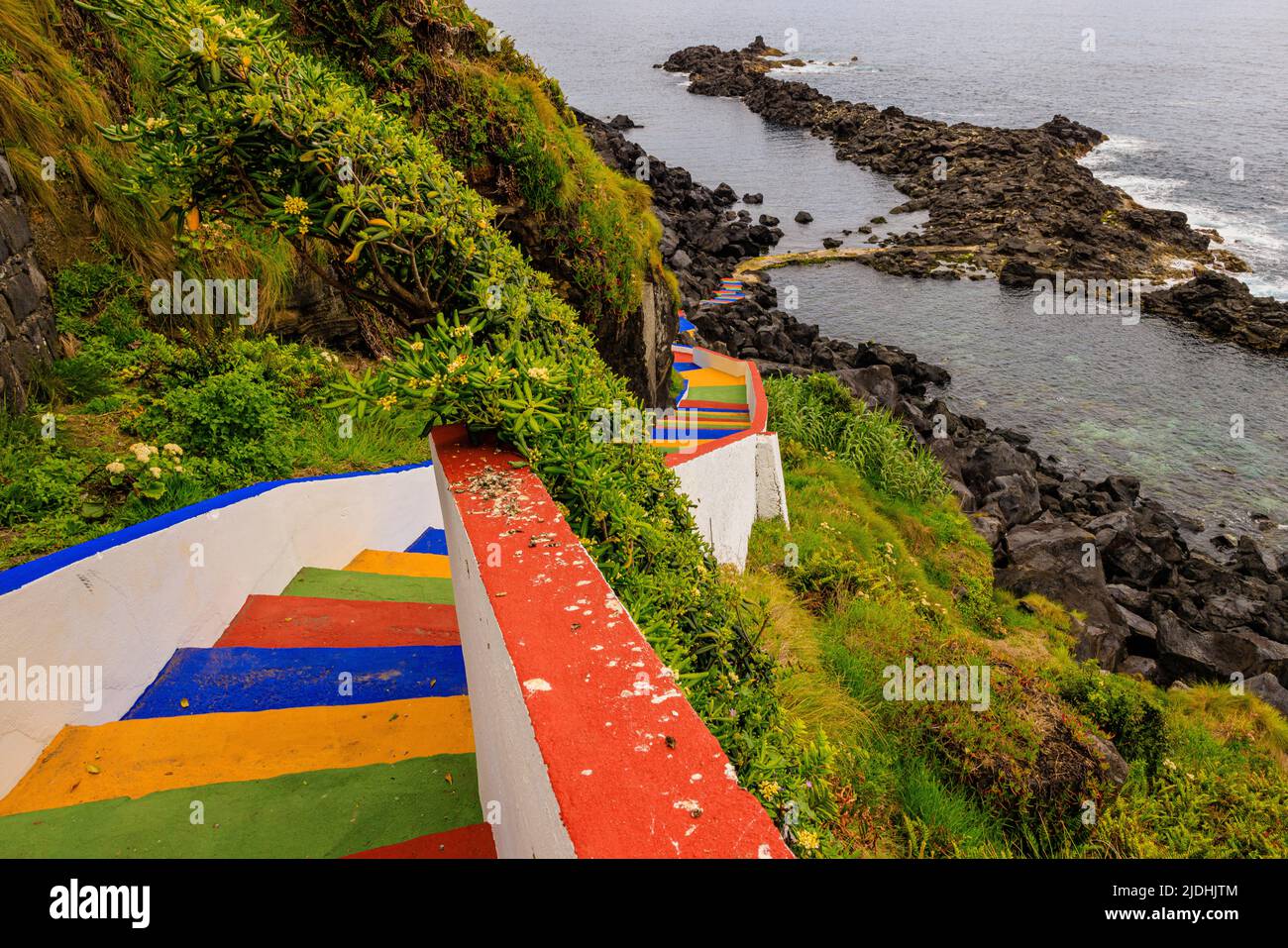 rainbow steps wind their way down to black volcanic rocks and calm sea at miradouro melo nunes Maia sao miguel azores Stock Photo