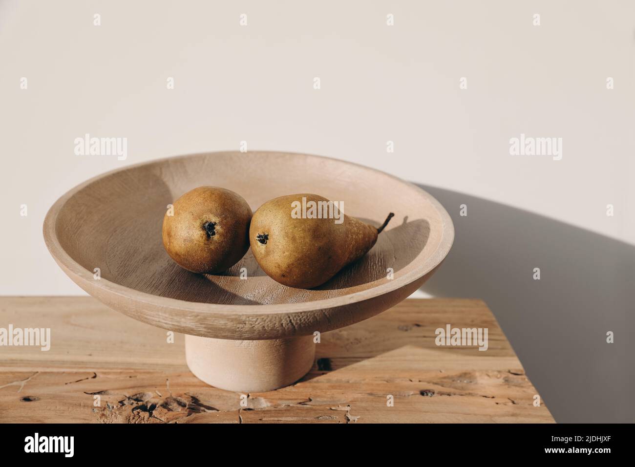 Autumn, summer fruit food still life. Couple of yellow pears, wooden bowl on table in sunset light. Blurred beige wall background, long shadows. Selec Stock Photo