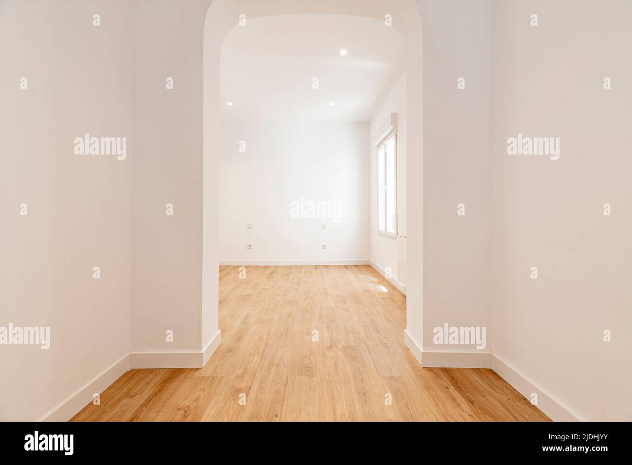 Empty room with plain white painted walls, plain aluminum windows and basket-handle arch separating the rooms with light oak wood floors Stock Photo