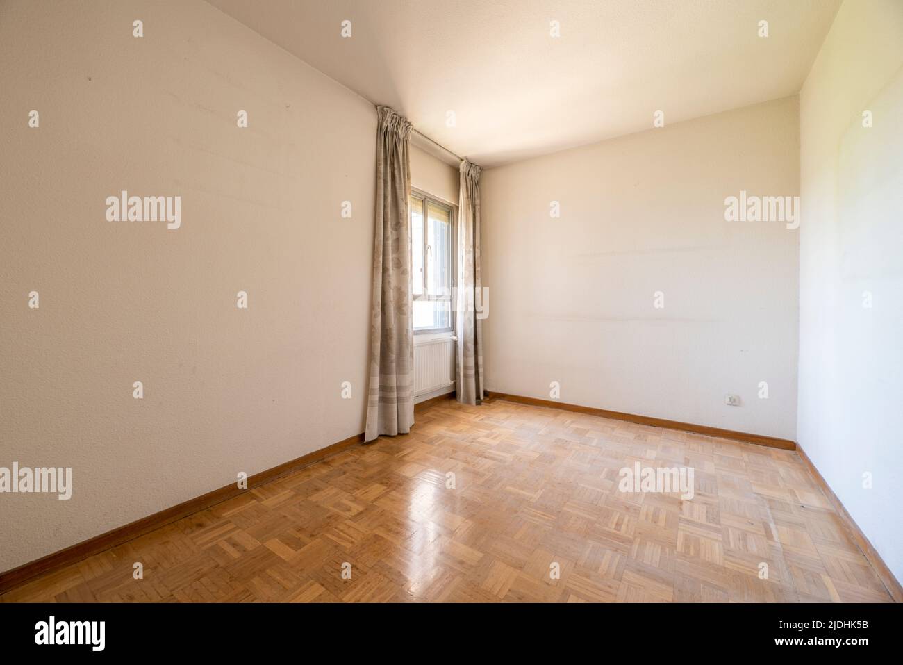Empty room with oak parquet floor and woodwork and window with curtains Stock Photo