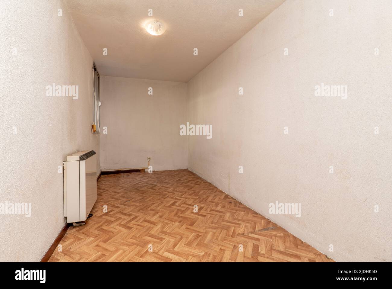 Empty room with herringbone oak parquet flooring and wood carpentry and heat accumulator on the wall Stock Photo