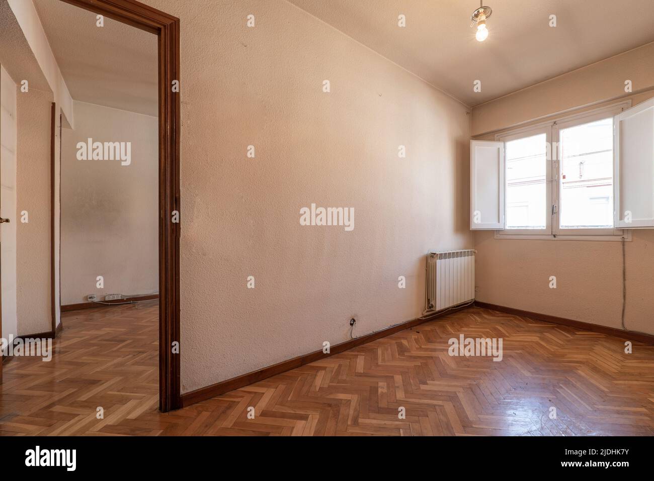 Empty room with bright oak parquet floor, white painted walls and reddish woodwork on white wooden doors and windows with shutters Stock Photo