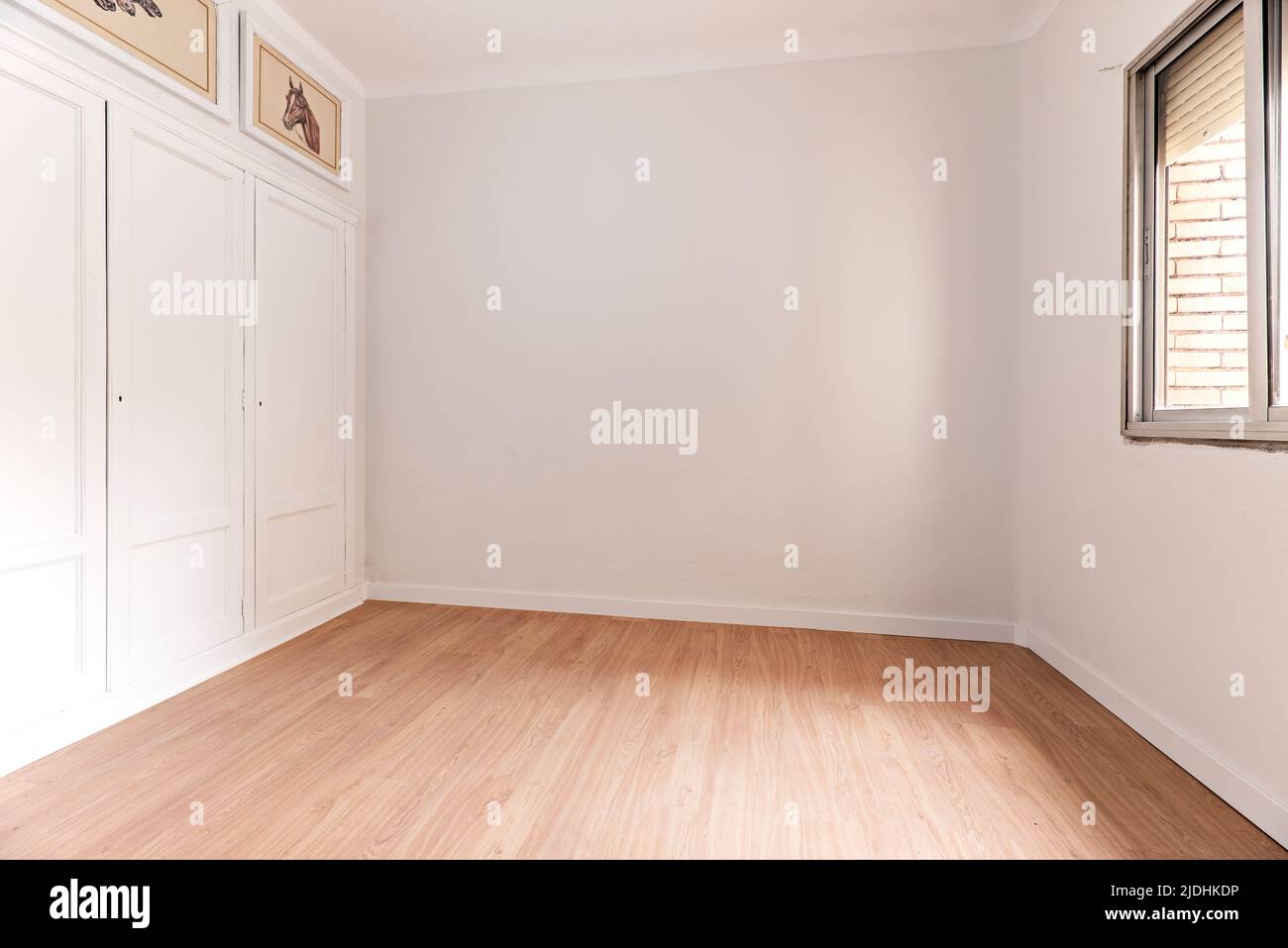 Empty room with oak parquet floor, white painted walls, built-in wardrobe with wooden doors and aluminum window Stock Photo