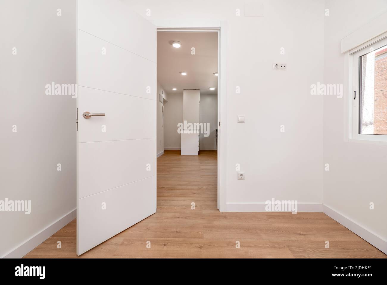 Empty room with oak parquet floor, white painted walls, access to another room and white aluminum windows Stock Photo
