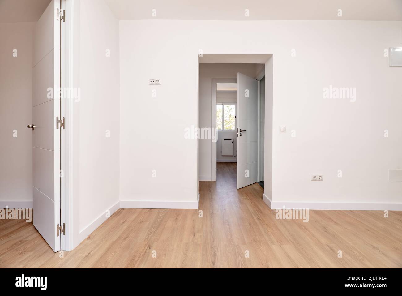 Empty living room with plain white painted walls, several access doors to other rooms with aluminum windows, white carpentry, doors and lamps and ligh Stock Photo