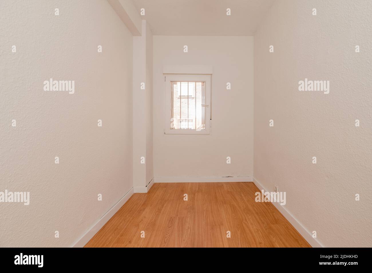 Small empty room with light wooden floors, white carpentry wood and white aluminum window Stock Photo