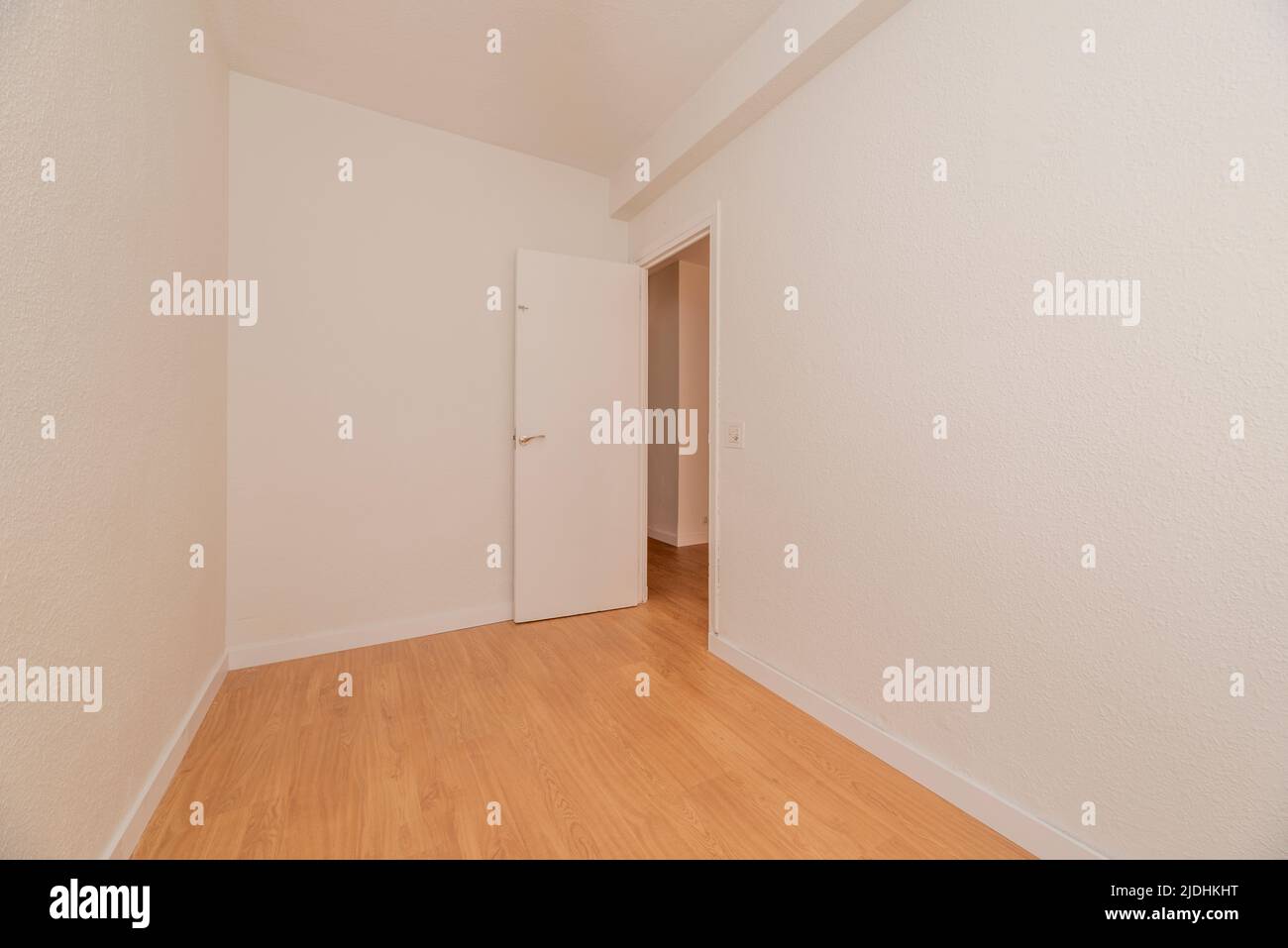 Small empty room with light wood flooring, white woodwork and white wood door Stock Photo