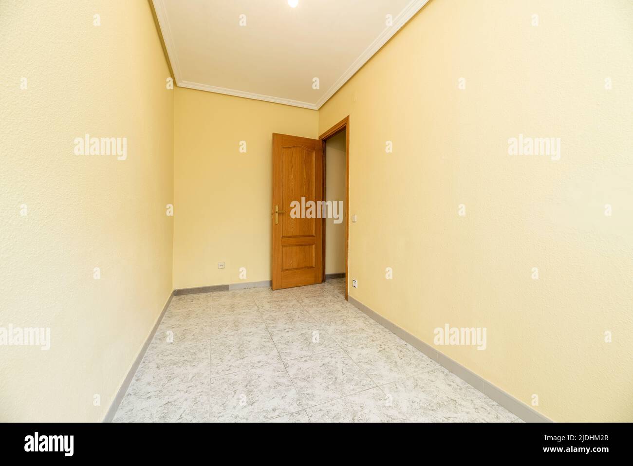 Empty room with stoneware floors, yellow painted walls and pine wood door Stock Photo