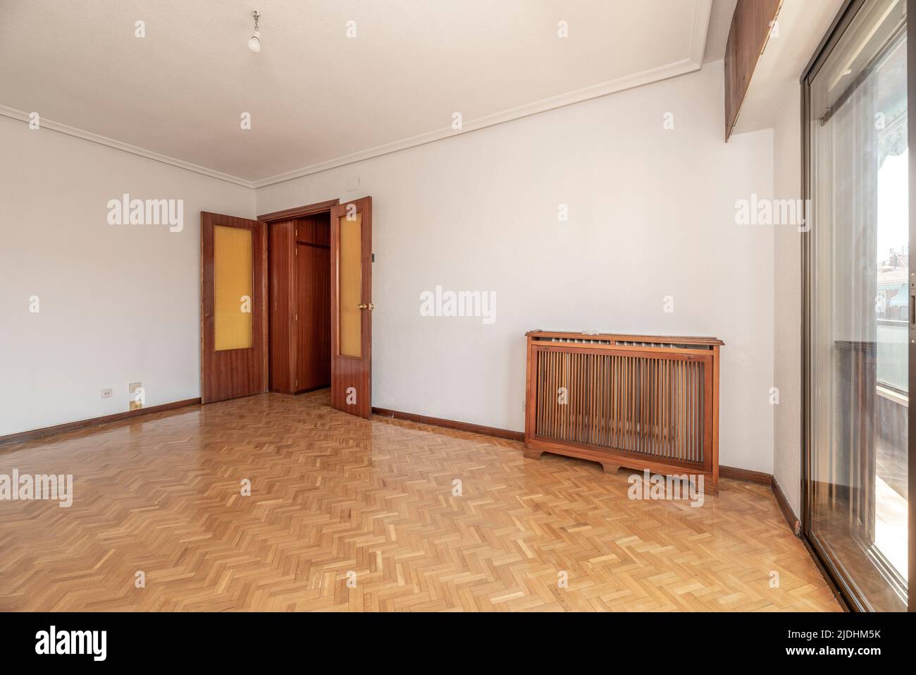 Empty living room with herringbone oak parquet floor, wooden radiator cover, white painted walls and brown aluminum joinery Stock Photo