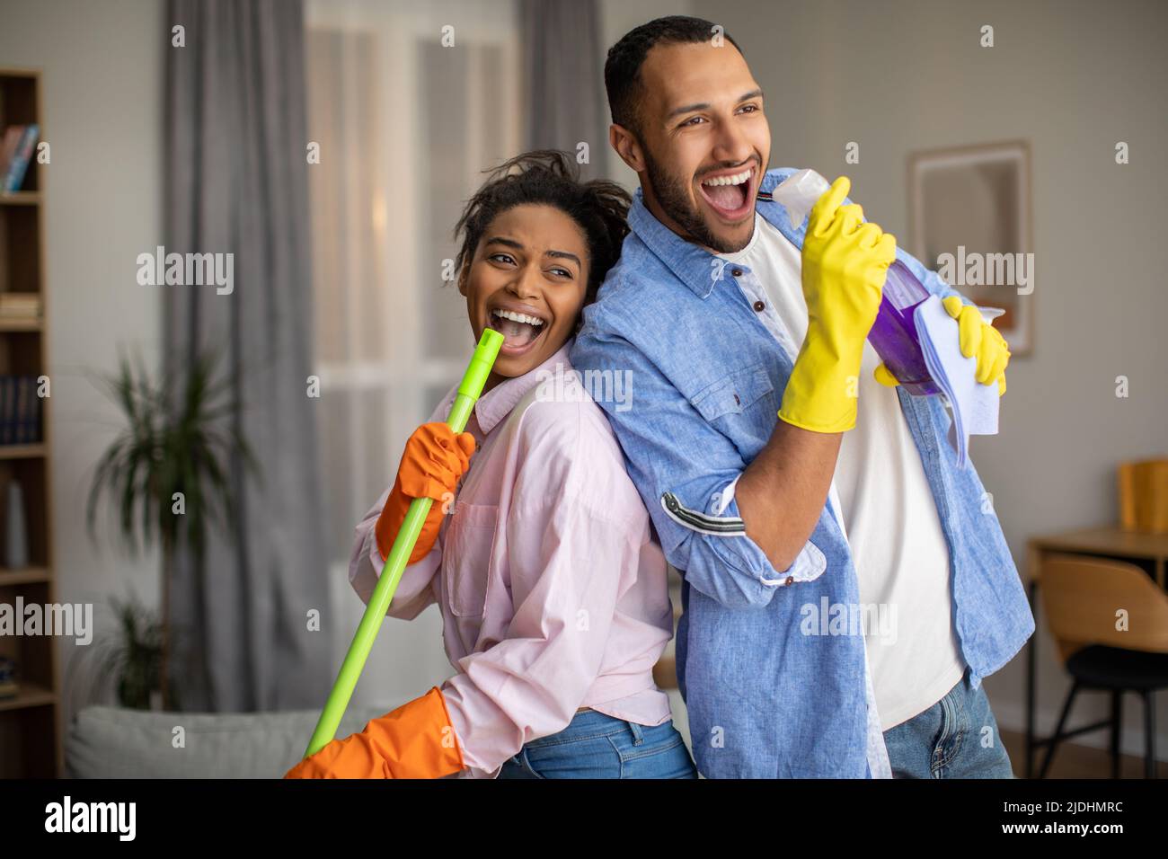 Joyful Black Couple Having Fun Cleaning House And Singing Indoor Stock Photo