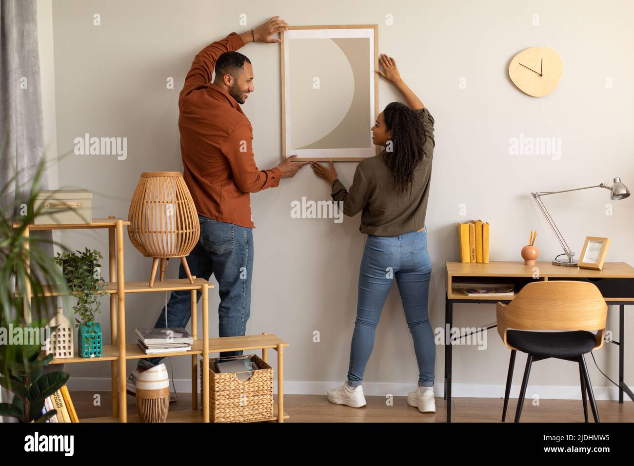 Black Millennial Spouses Hanging Poster On Wall Together At Home Stock