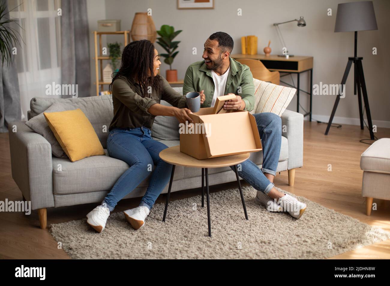 Excited Black Couple Unpacking Box With Delivered Items At Home Stock Photo