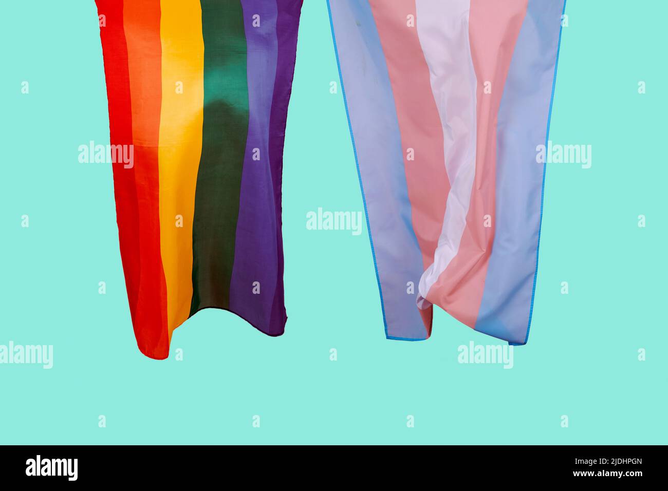 the gay pride flag and the transgender pride flag waving in the air on a greenish blue background Stock Photo