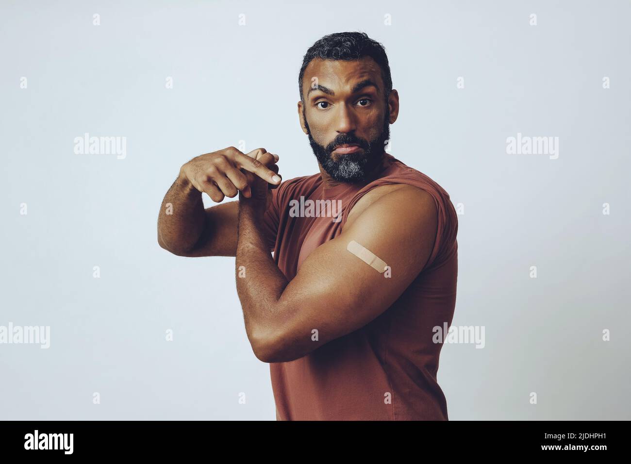 portrait mid adult bearded vaccinated man in the studio flexing arm muscle and pointing at plaster studio shot Stock Photo