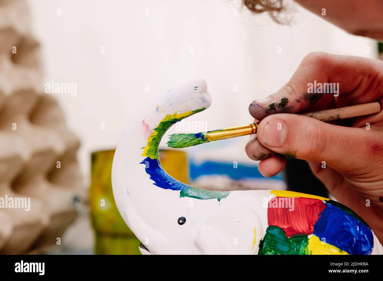 Child plays to unleash his creativity by decorating a white plaster figure with colored paints, during the summer holidays. Stock Photo