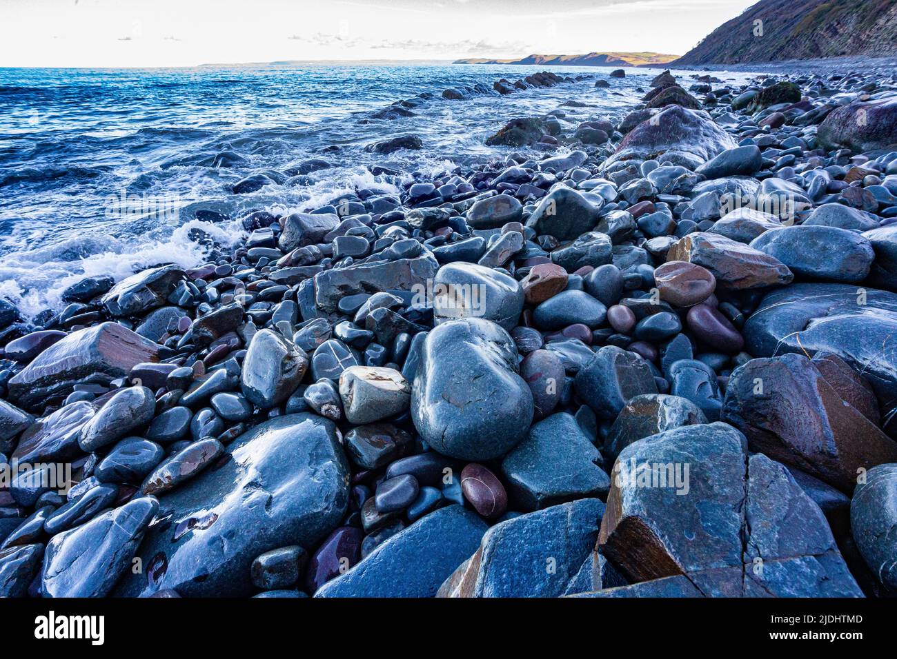 Colourful Wet Rocks Detail on Bucks Mills Beach at High Tide with View of the Beach and North Devon Coastline,  Bucks Mills, Devon, Great Britain. Stock Photo