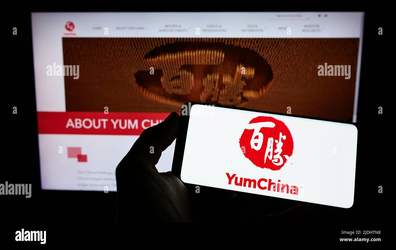 Person holding smartphone with logo of restaurant company Yum China Holdings Inc. on screen in front of website. Focus on phone display. Stock Photo