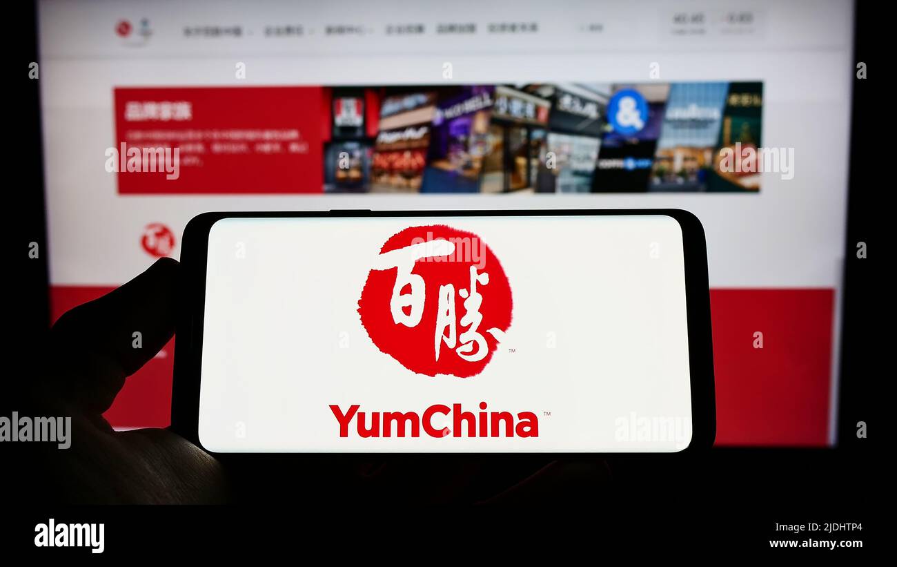 Person holding mobile phone with logo of restaurant company Yum China Holdings Inc. on screen in front of web page. Focus on phone display. Stock Photo