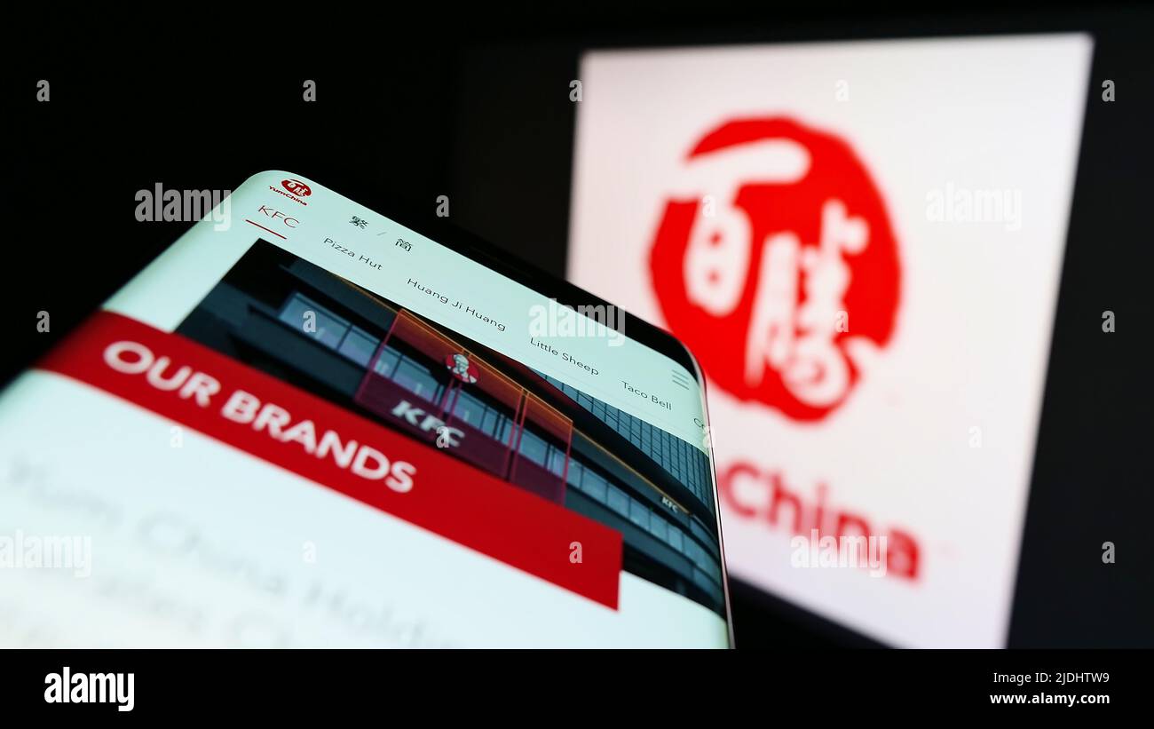 Mobile phone with website of restaurant company Yum China Holdings Inc. on screen in front of buinsess logo. Focus on top-left of phone display. Stock Photo