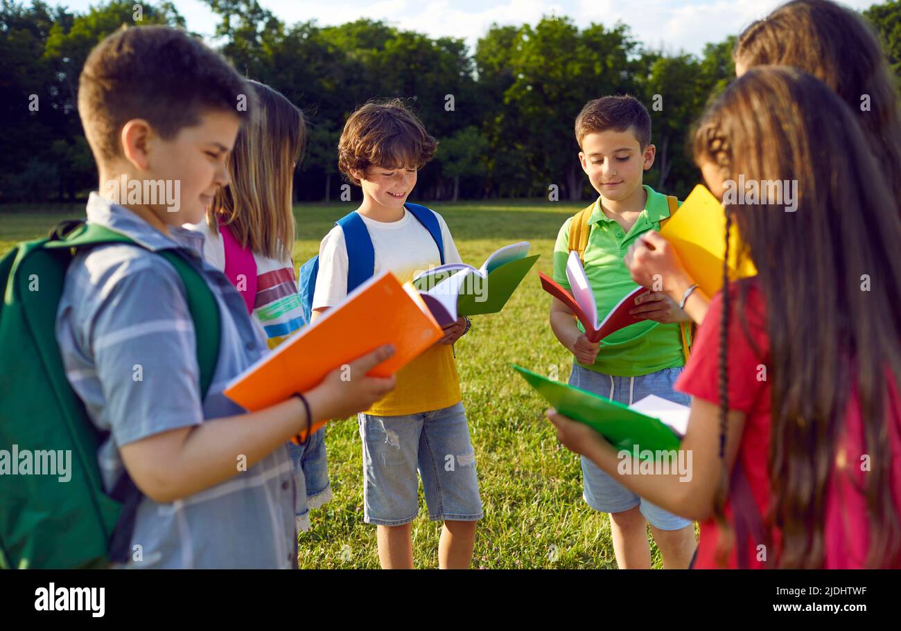 Group of elementary school students read books together standing in circle in park near school. Stock Photo