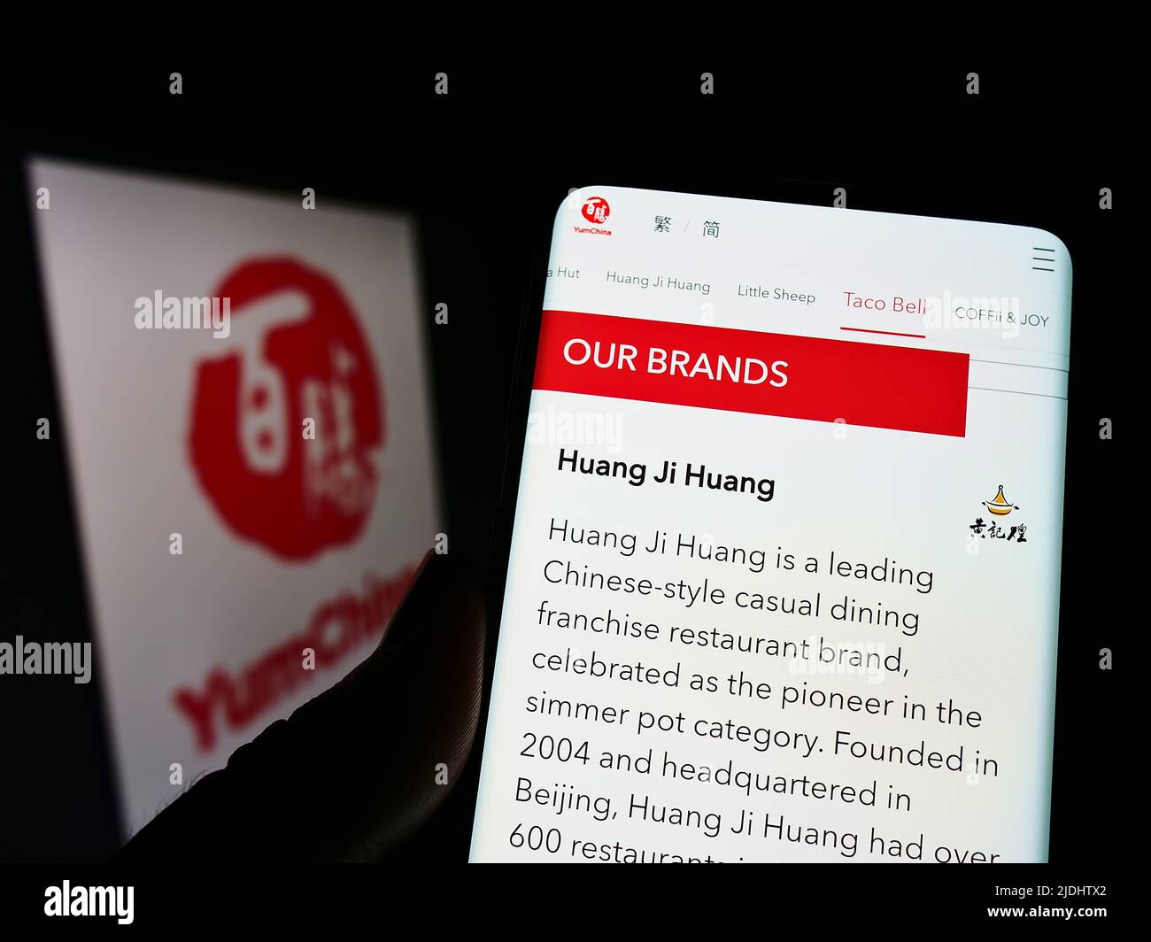 Person holding cellphone with webpage of restaurant company Yum China Holdings Inc. on screen in front of logo. Focus on center of phone display. Stock Photo