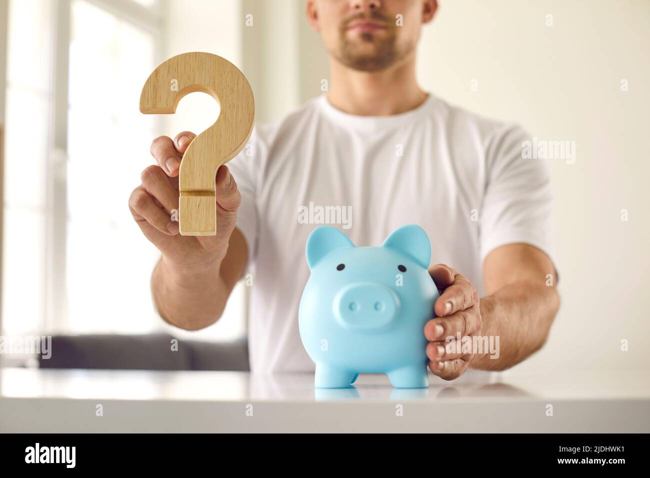 Man who is thinking about what currency to keep money holds question mark near piggy bank. Stock Photo