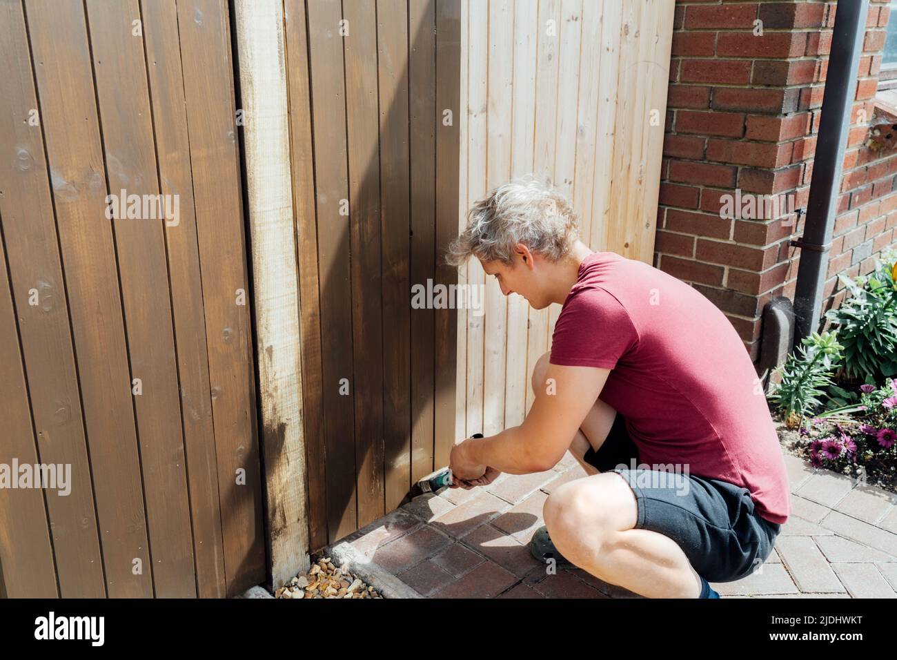 Young man worker paints with a brush a wooden board fence gate. DIY, Do