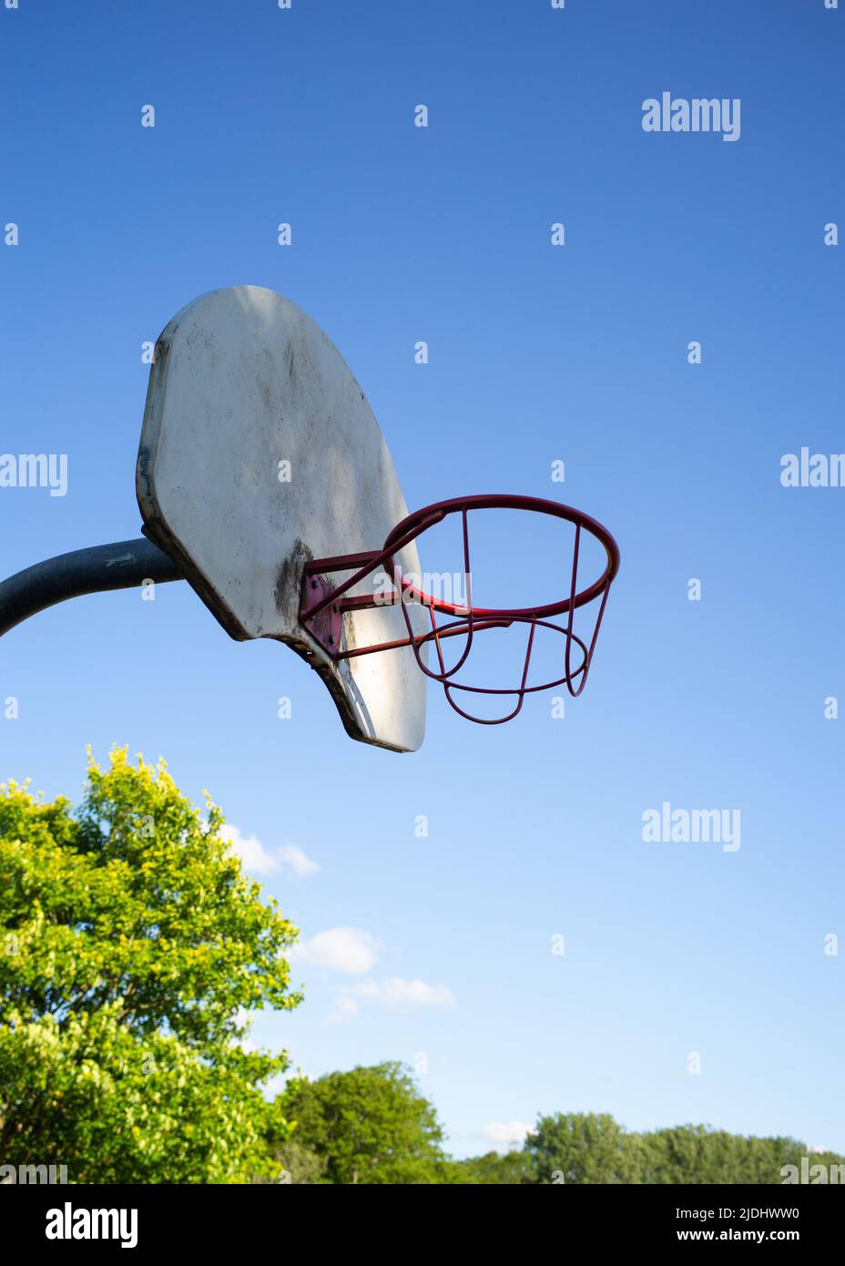 Metal basketball hoop and board against a cloudless strong blue sky with copy space. lit with dappled sunlight. Stock Photo