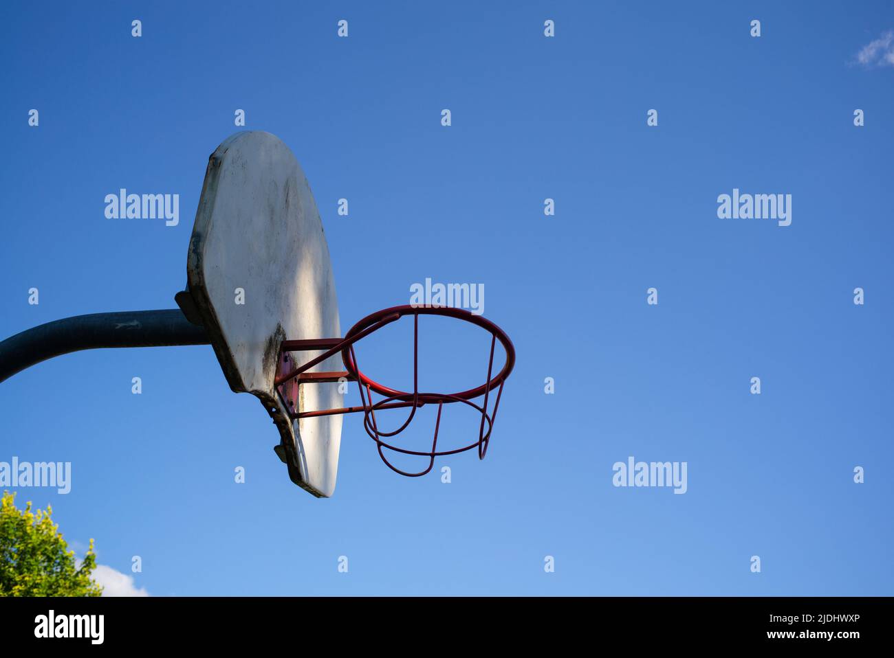 Metal basketball hoop and board against a cloudless strong blue sky with copy space. lit with dappled sunlight. Stock Photo