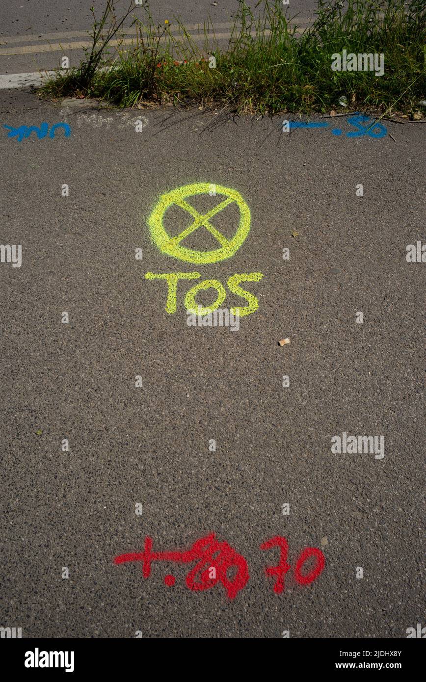 A yellow spray paint marking on public pavement with the letters TOS alongside a circle with a cross inside. Stock Photo