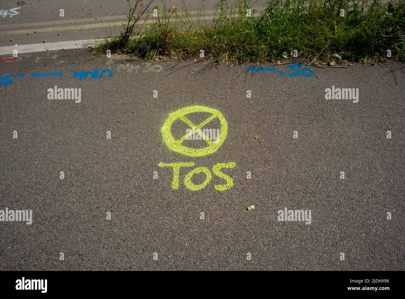 A yellow spray paint marking on public pavement with the letters TOS alongside a circle with a cross inside. Stock Photo
