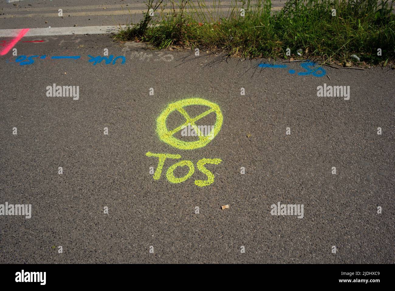 A yellow spray paint marking on public pavement with the letters TOS alongside a circle with a cross inside. Stock Photo