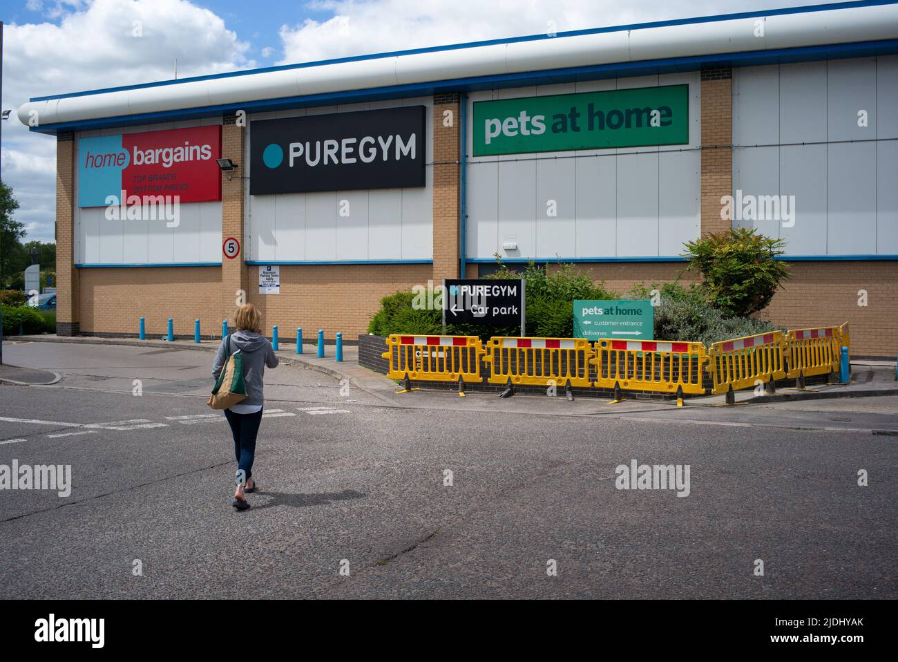 A women walks towards an out of town retail unit site in Salisbury Wiltshire UK, signage with home bargains, pure gym and pets at home showing. Stock Photo