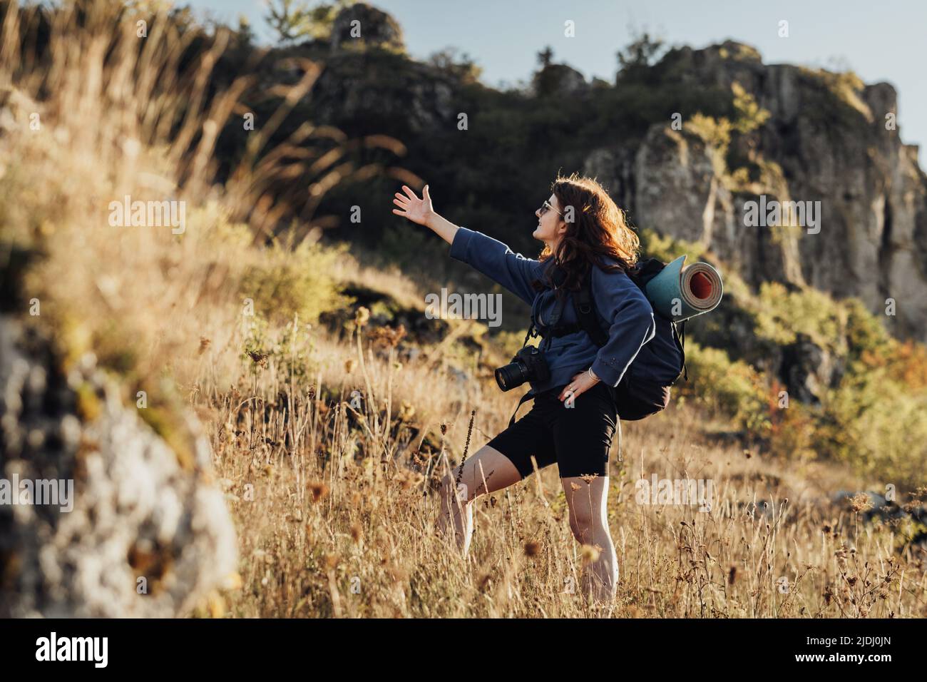 Travel Young Woman with Backpack and Camping Mat and Wearing Digital Camera on a Strip and