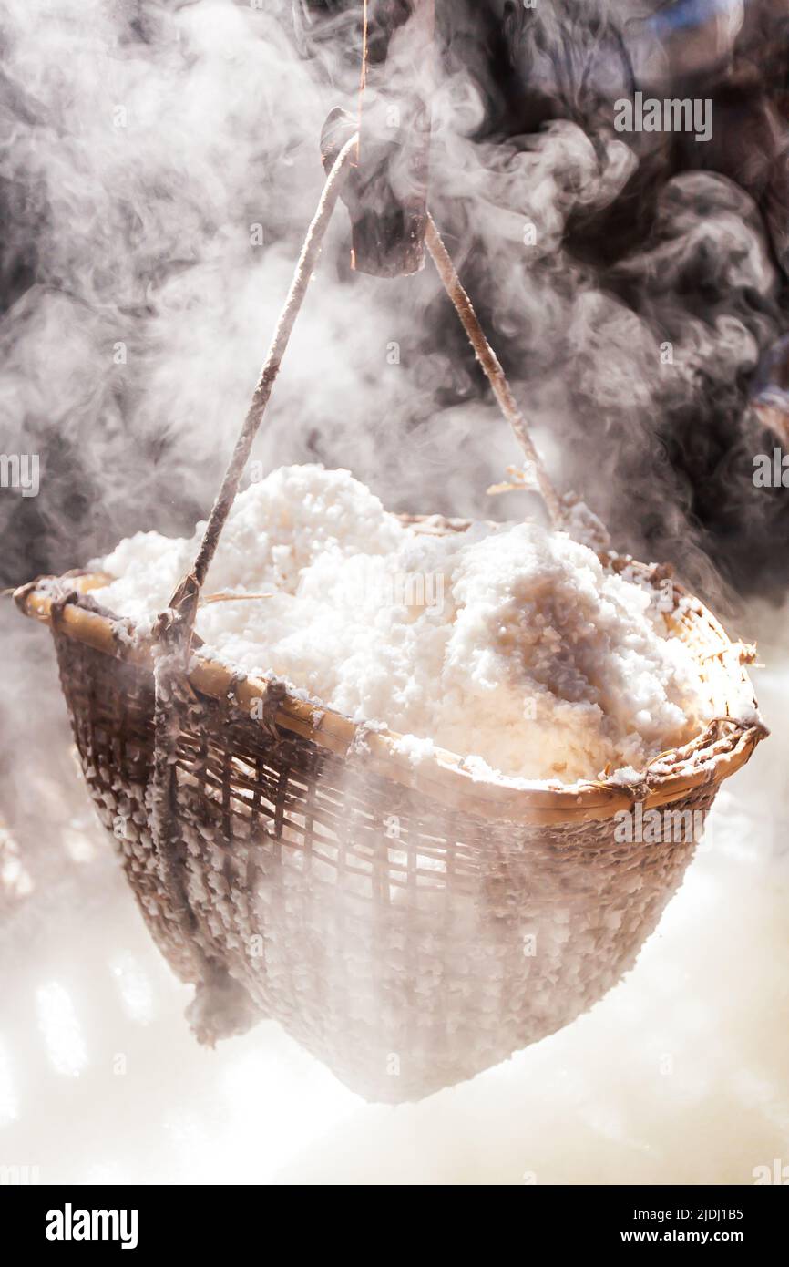 Boiling rock salt on firewood oven. Salt is still produced in the traditional way in Bo Kluea, Thailand. Focus on the bamboo basket of rock salt. Stock Photo