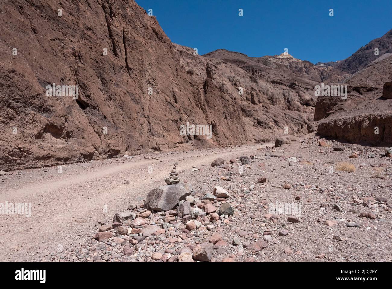 Rock cairn beside wide trail leading into Natural Bridge Canyon in Black Mountains (shown in distance) of Death Valley National Park. Stock Photo