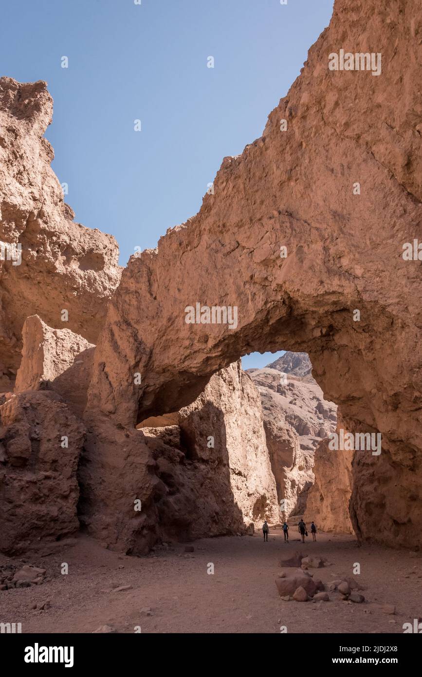 A family of four people hiking under the Natural Bridge arch in the popular canyon for short day hikes at Death Valley National Park in California. Stock Photo