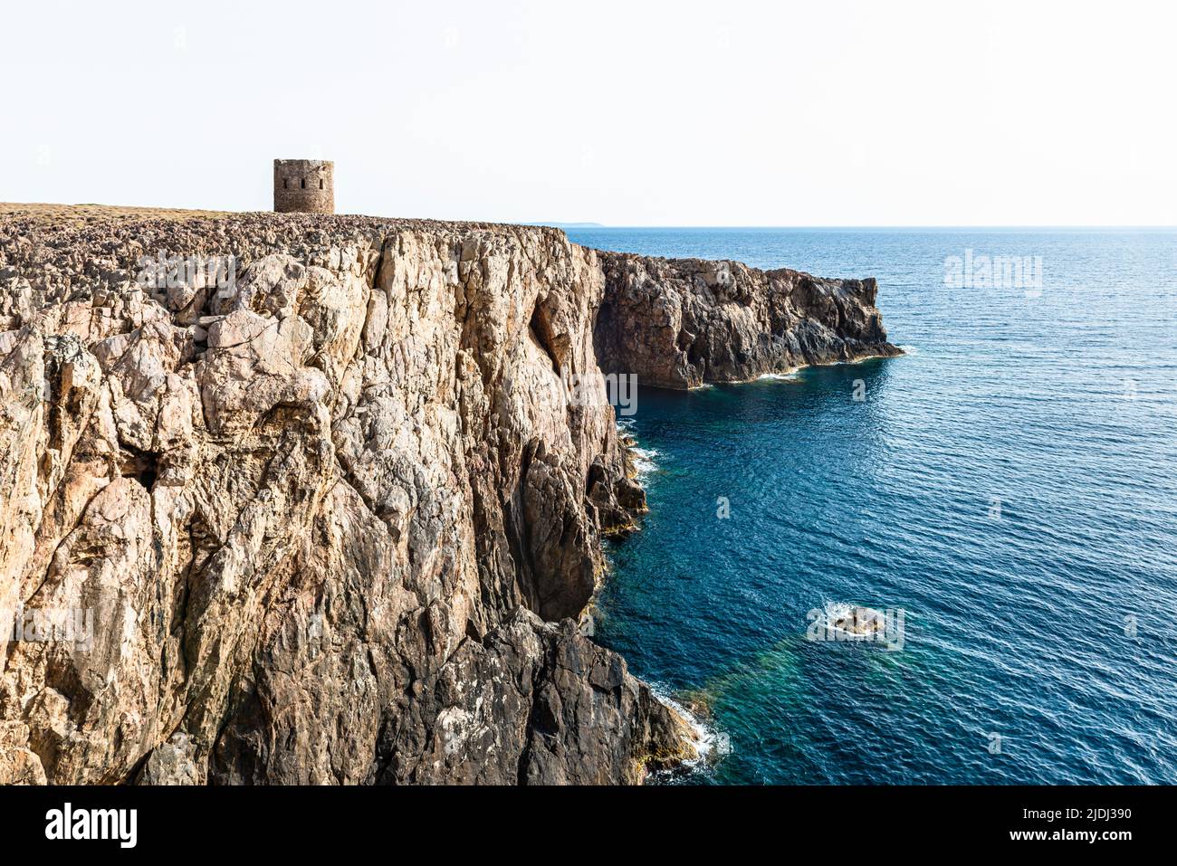 The derelict coastguard tower Torre Spagnola on the rugged karst rocks of the cliff at Cala Domestica, Iglesiente, Sardinia, Italy Stock Photo