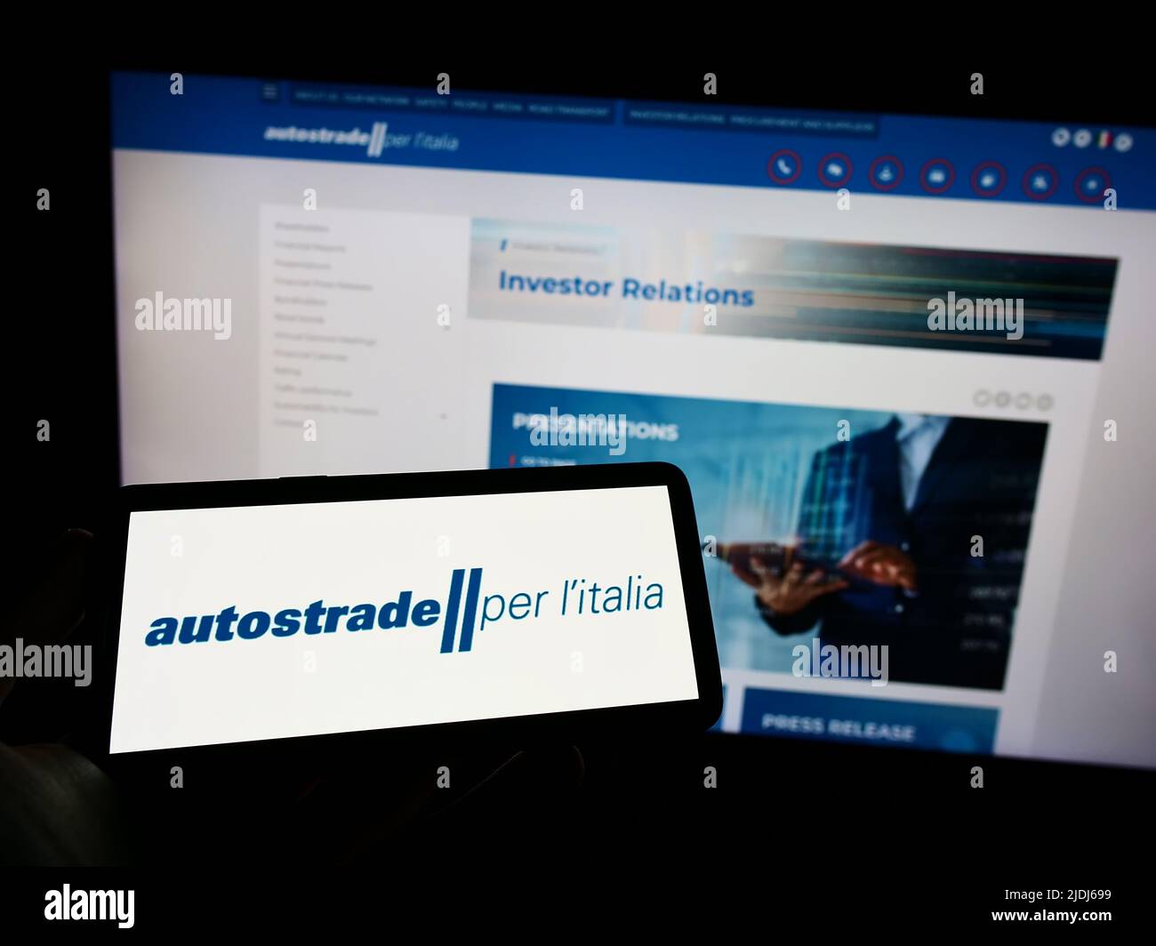 Person holding mobile phone with logo of motorway company Autostrade per l'Italia S.p.A. on screen in front of web page. Focus on phone display. Stock Photo