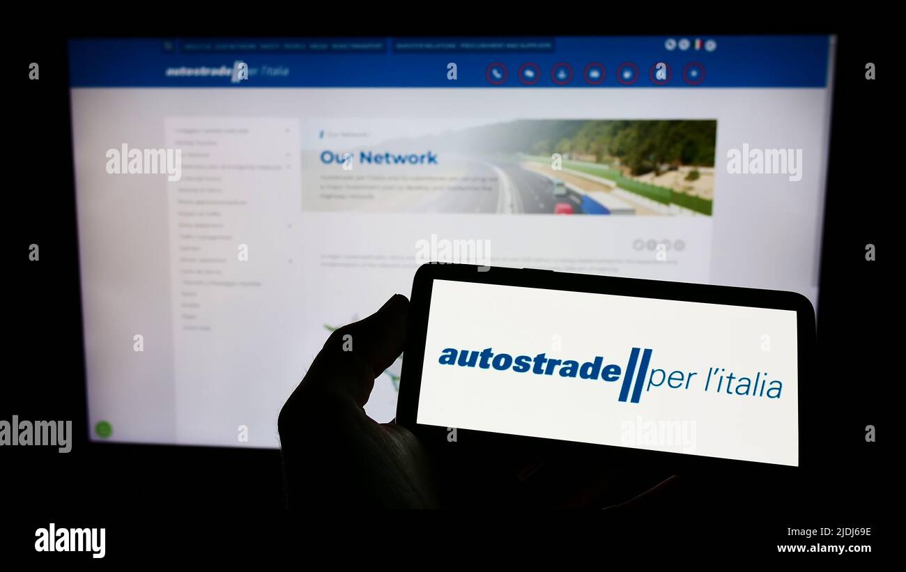 Person holding cellphone with logo of motorway company Autostrade per l'Italia SpA on screen in front of business webpage. Focus on phone display. Stock Photo