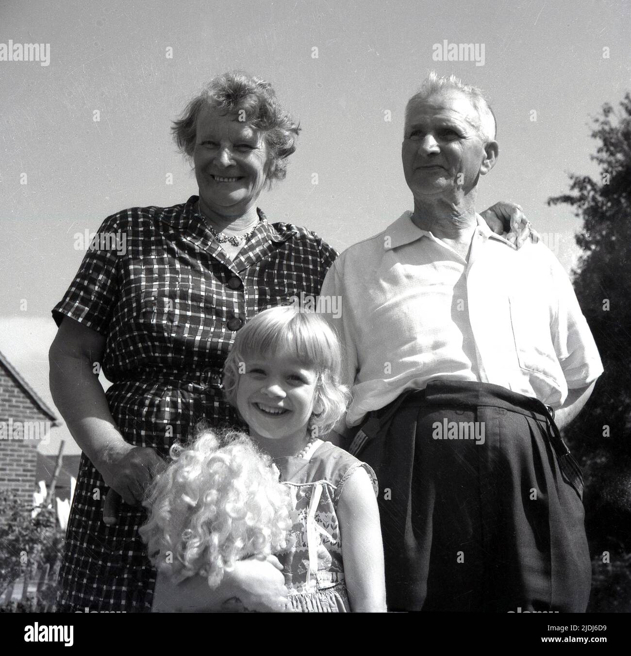 1960s, historical, all smiles, a happy young girl standing outside with her grandparents holding her doll, England, UK. Stock Photo