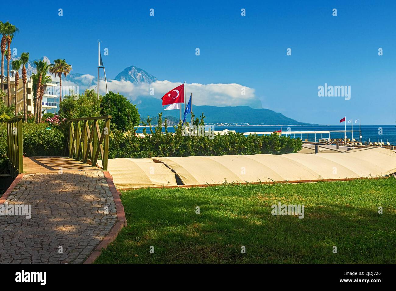 View of the path and the bridge in a green garden with green trees along the embankment in Kemer, Turkey. Stock Photo